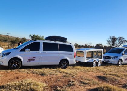 the image shows three vehicles belonging to Ithemba Elitjha Funeral services. The main vehicle in the picture is a white Mercedes Benz V-class passenger car branded with Ithemba Elitjha branding and behind it, there's a coffin carriage