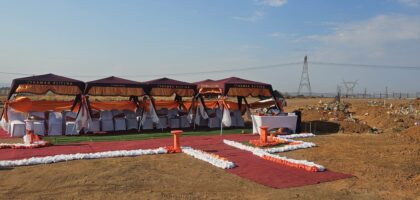 the image shows graveside Ithemba Elitjha deco. There are four maroon branded gazebos with a large number of white covered chairs underneath, all on the red carpet with orange and white grave side decorations.