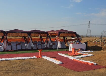 the image shows graveside Ithemba Elitjha deco. There are four maroon branded gazebos with a large number of white covered chairs underneath, all on the red carpet with orange and white grave side decorations.