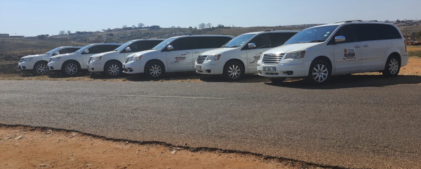 The image shows six white cars belonging to Ithemba Elitjha Funeral services parked on the side of a road in Mpumalanga. They are branded with the Ithemba Elitjha magnetic stickers