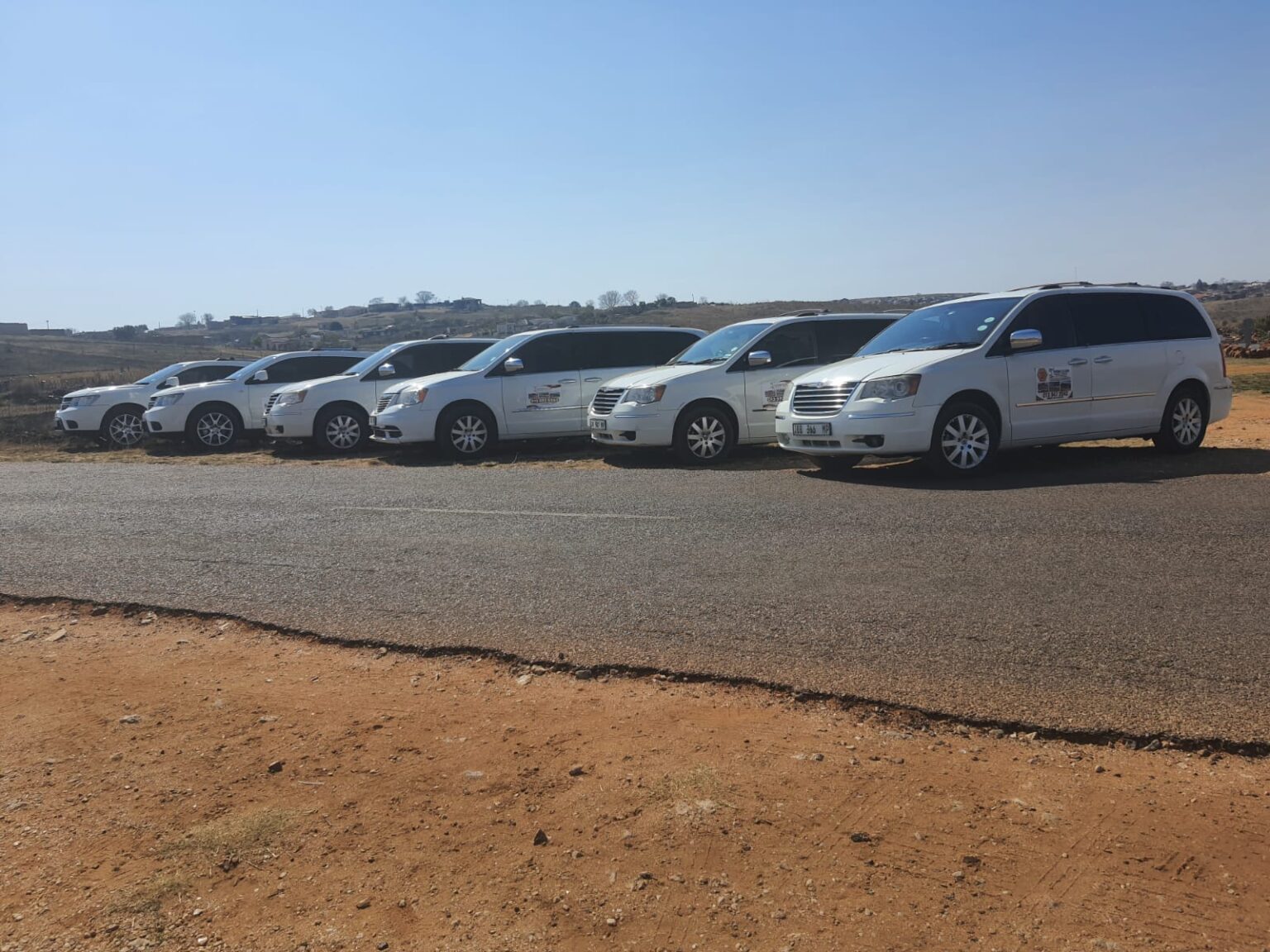 The image shows six white cars belonging to Ithemba Elitjha Funeral services parked on the side of a road in Mpumalanga. They are branded with the Ithemba Elitjha magnetic stickers