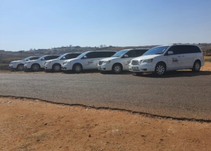 The image shows six white cars belonging to Ithemba Elitjha Funeral services parked on the side of a road in Mpumalanga. They are branded with the Ithemba Elitjha magnetic stickers